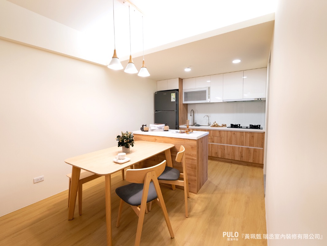隨著木地板的紋路延伸，來到另一頭的廚房空間，以純白及木紋作為主要風格，溫柔地將色彩填滿廚房檯面，每一處都可見木紋展露的質感，而中島的設計更帶提高廚房實用性，連貫了一家團聚的美好。瑞丞室內裝修有限公司木作裝潢作品 - PULO裝潢平台
